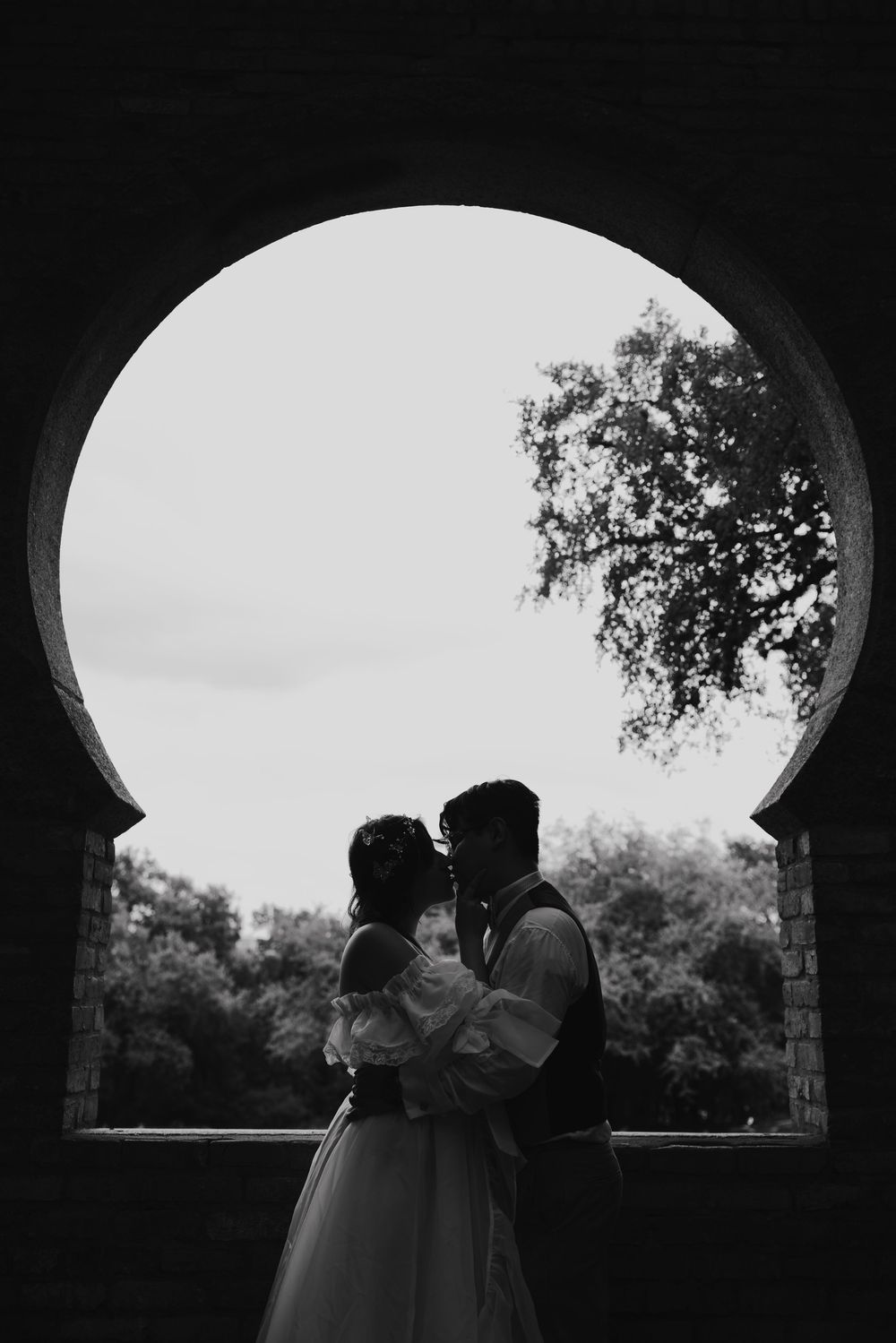 A silhouetted couple shares a romantic moment under an arched passageway at dusk.