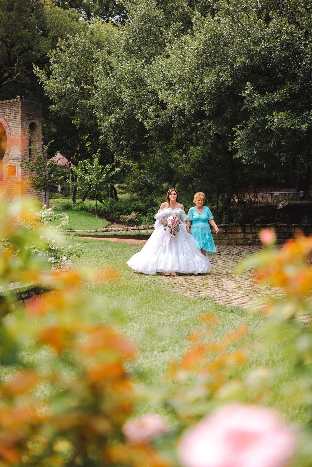 A couple sits in a garden surrounded by blurred orange and pink flowers on a sunny summer day.