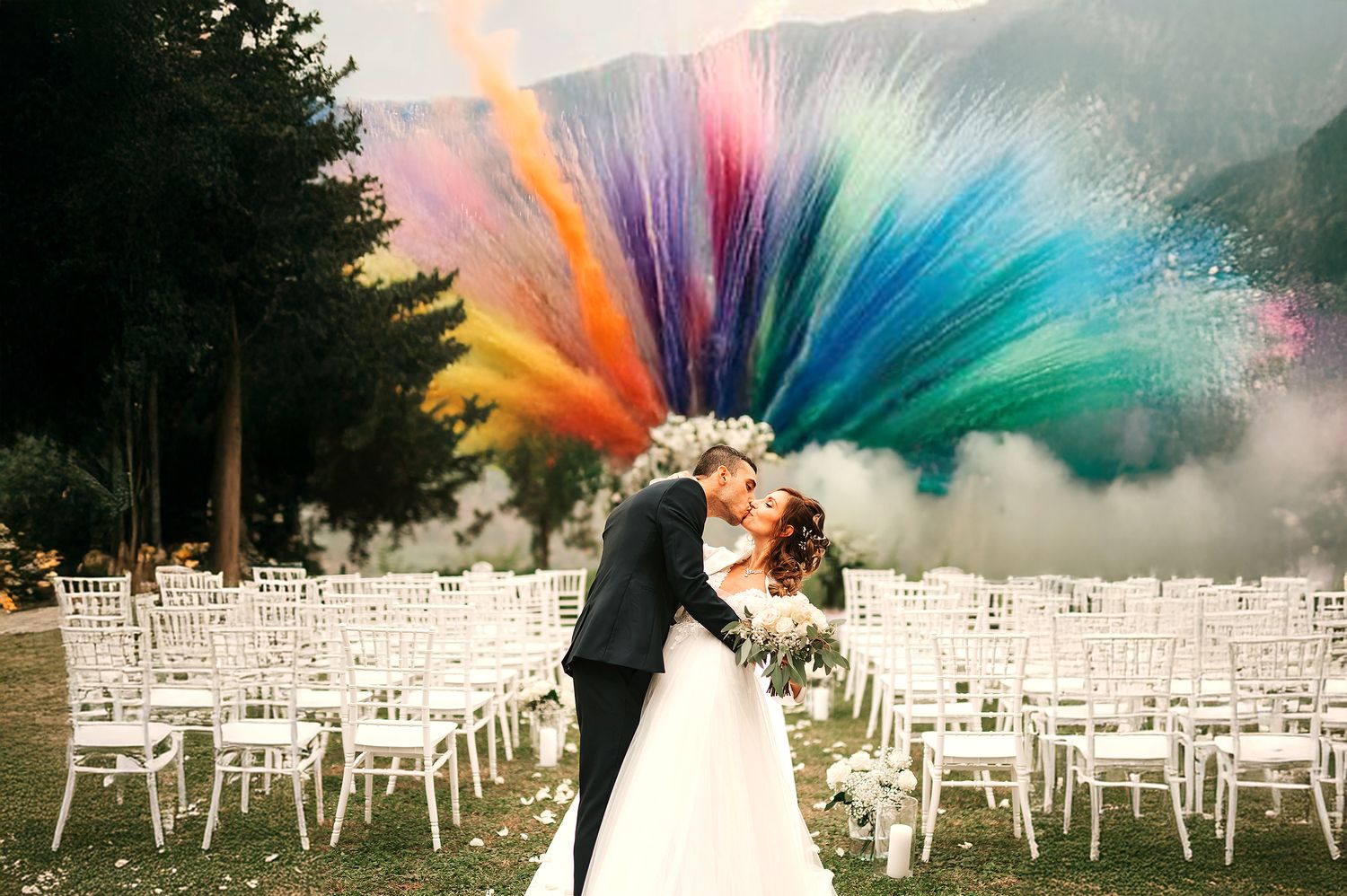 Wedding couple kissing under a stunning rainbow colored powder explosion at an outdoor ceremony venue.