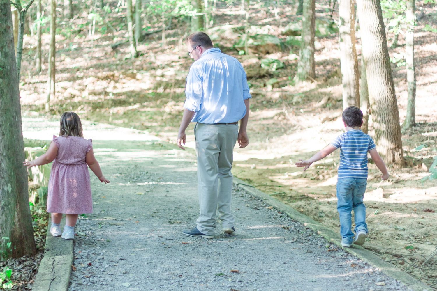 Children balancing on wood beams on side of pathway with dad in between