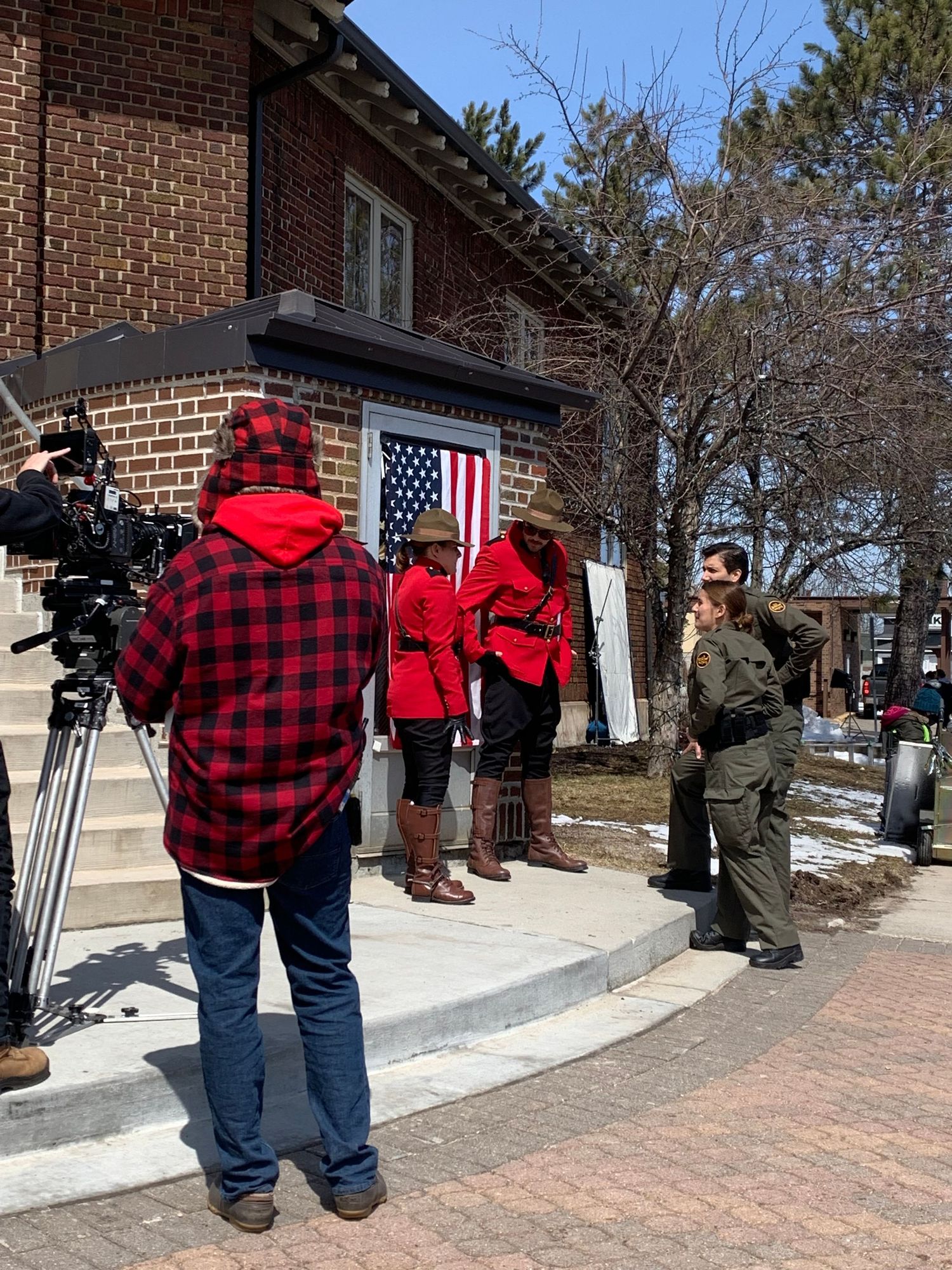 Film crew with cameras filming outside a brick house with American flag.