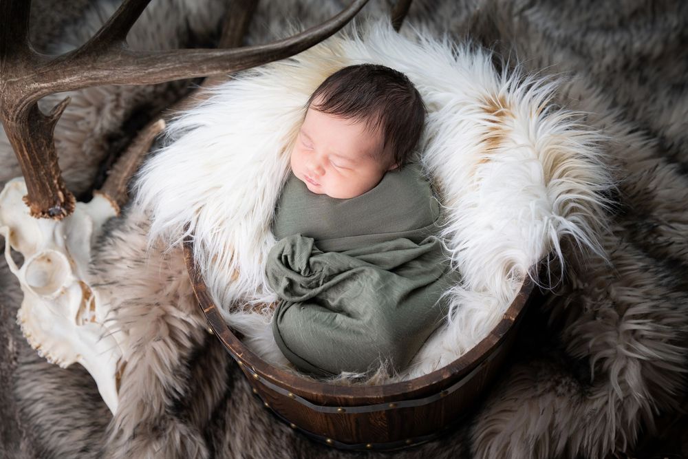 A sleeping infant nestled in cozy white fur blankets on a wooden surface.