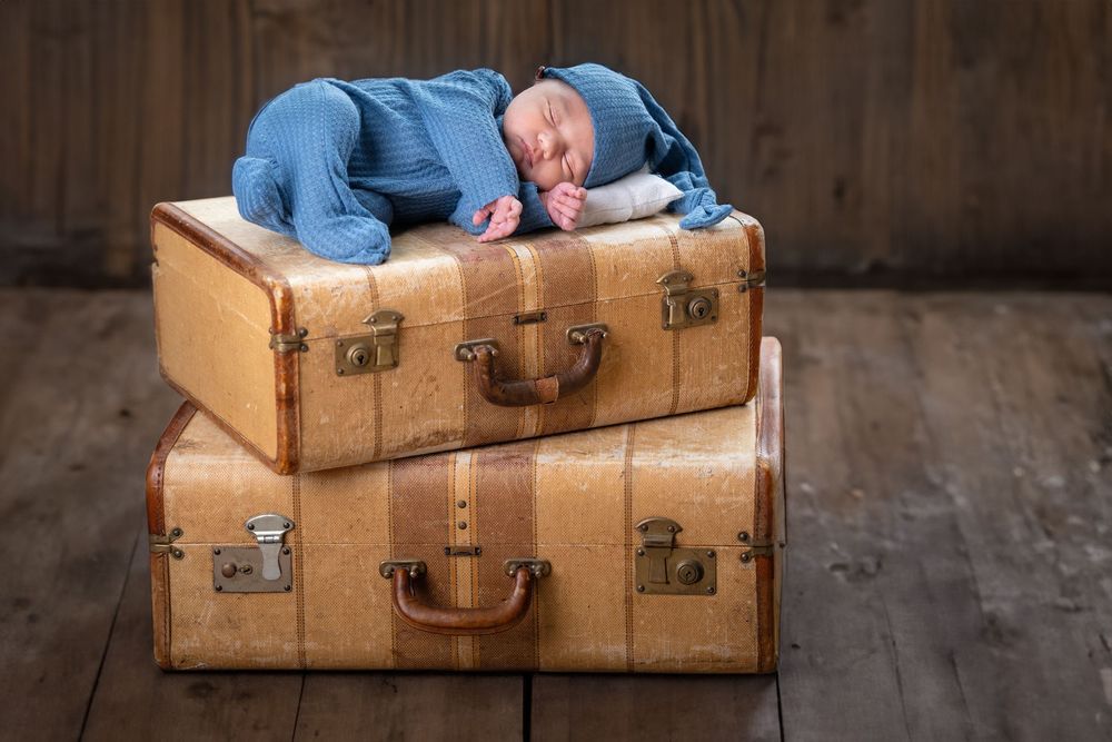 A newborn baby rests peacefully on vintage brown leather suitcases during a professional photo session.