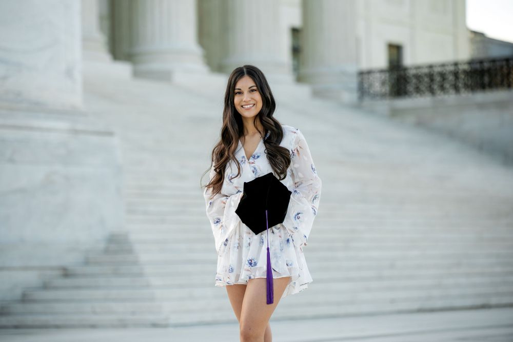 Female stands on marble steps wearing a floral white dress and holding a large black clutch purse near classical columns in Washington DC.