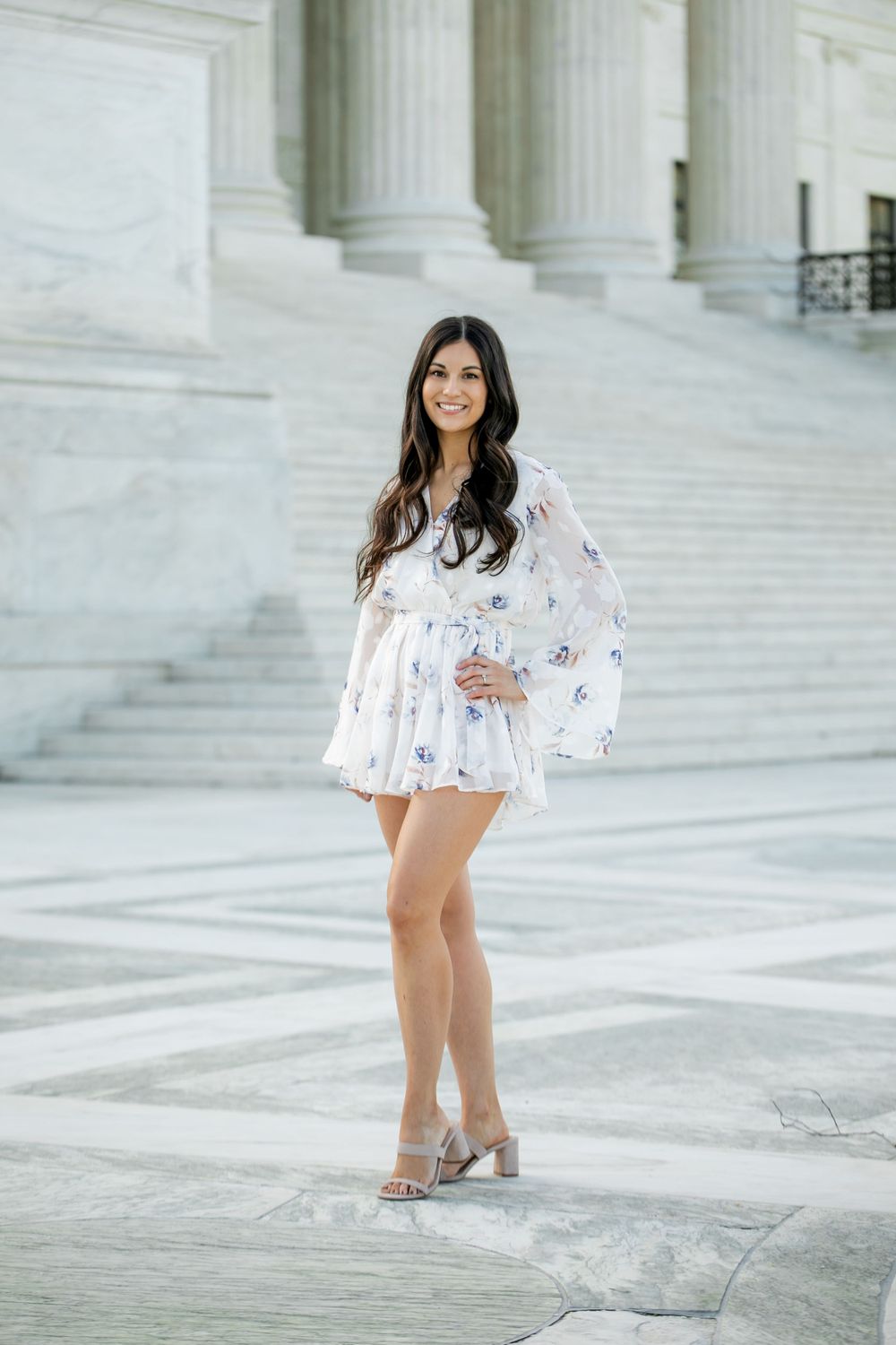 Woman in a flowing white floral dress with bell sleeves poses on marble steps of a grand building, by Justin Baker Photography. DMV.