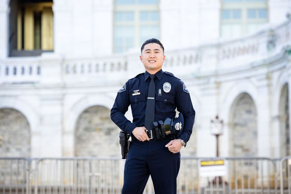 Smiling police officer in uniform standing confidently in front of a grand white building outdoors.