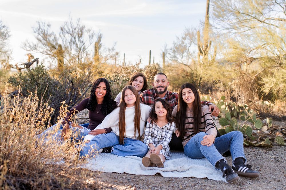 Family of six sitting on a blanket in a desert setting with warm golden light.