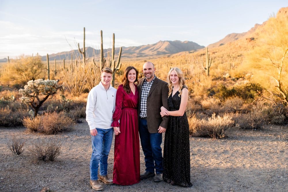 Family of four standing together in a desert landscape with saguaro cacti at sunset.