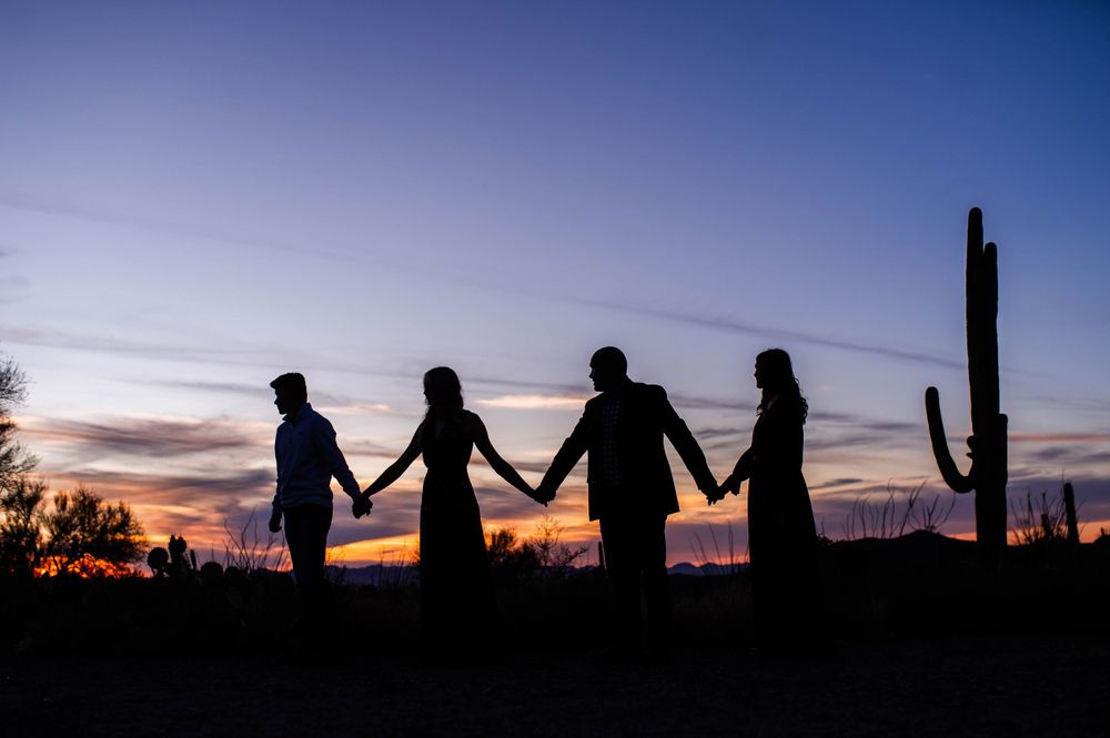 Silhouette of four family members holding hands at sunset next to a saguaro cactus in the desert.