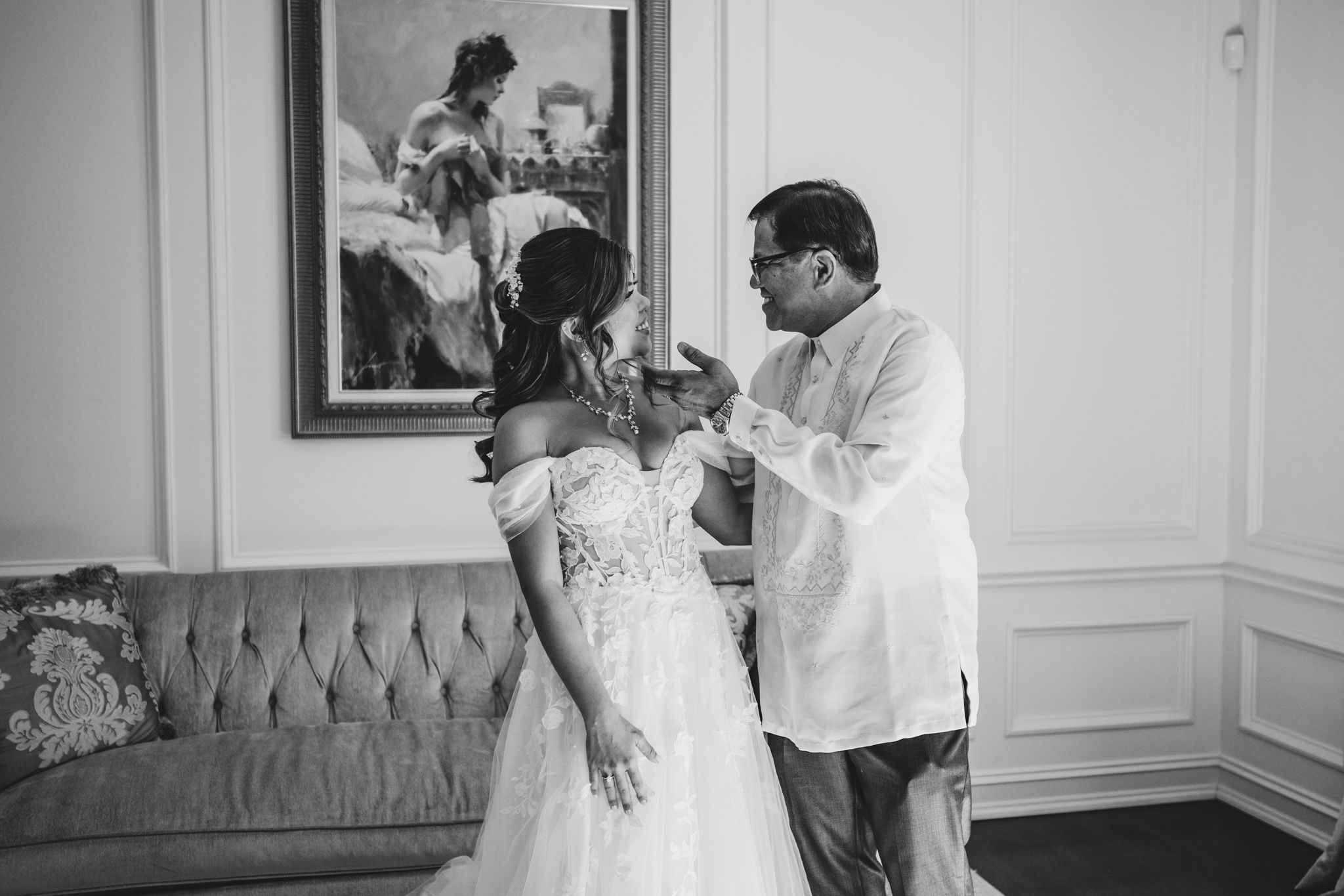 A black and white photo showing final wedding dress adjustments in an elegant room.