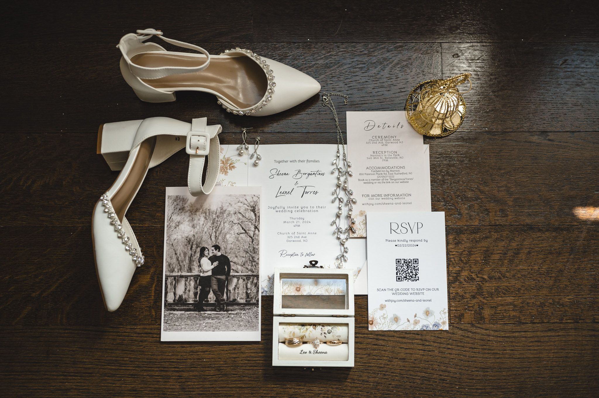 Wedding details including white bridal shoes, invitations, and accessories arranged on dark wooden surface.
