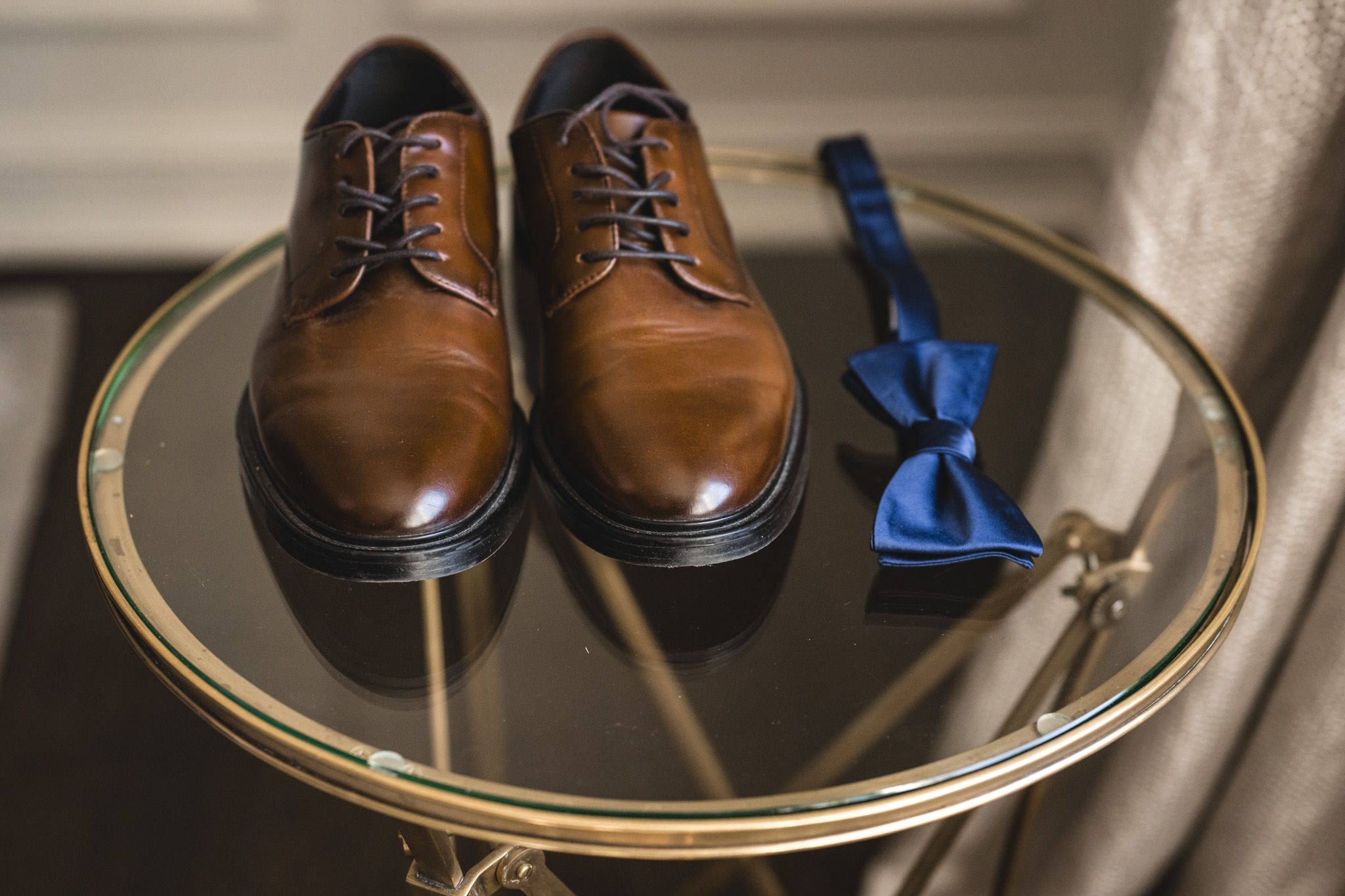 Brown leather dress shoes and blue bow tie displayed on a gold mirrored table.