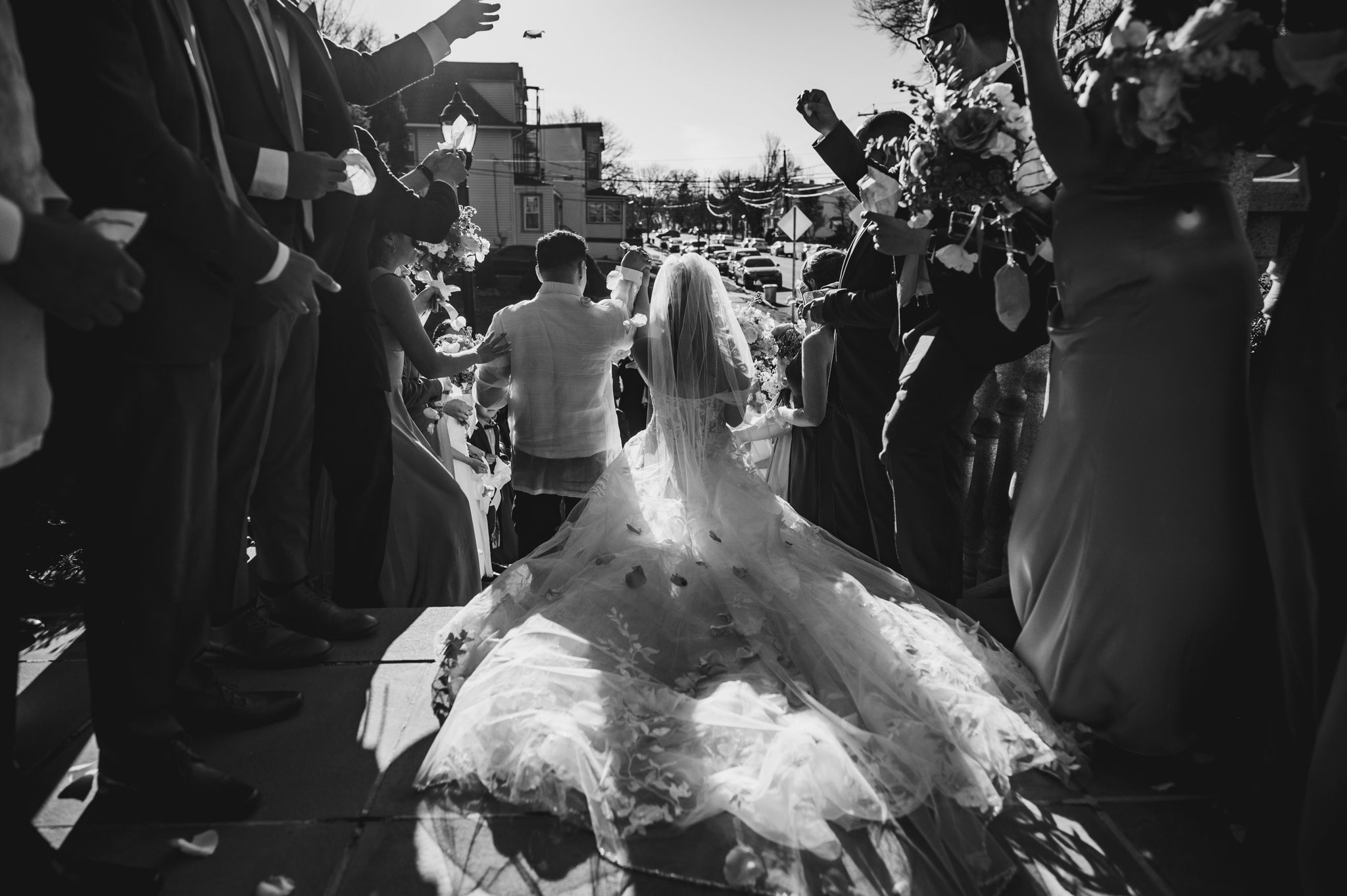 Black and white photo of a bride in flowing dress walking through crowd of guests.