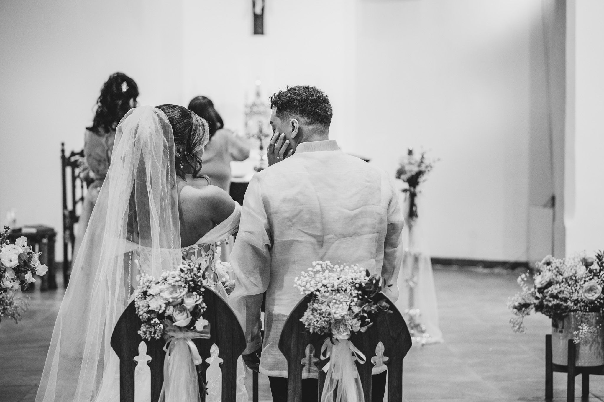 Black and white photo of a couple kneeling at church altar during their wedding ceremony.
