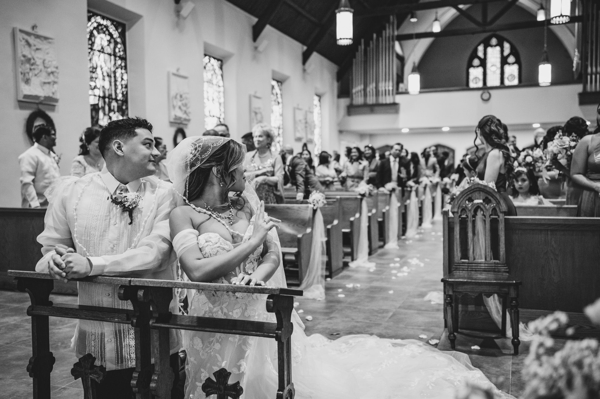 Black and white photo showing wedding guests seated in wooden church pews during ceremony.