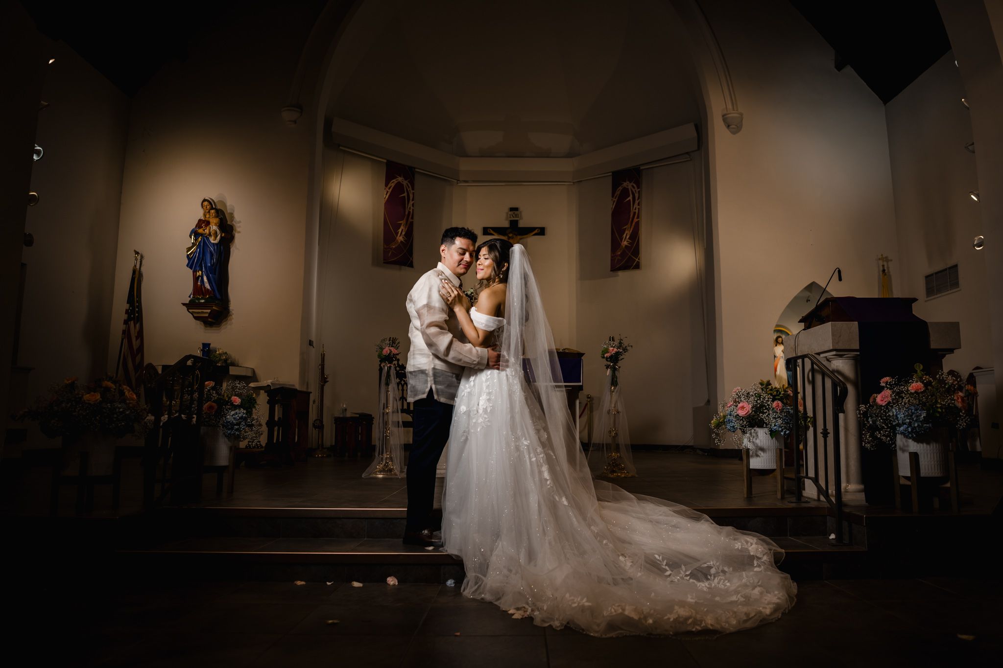 Dramatic wedding portrait in dimly lit church with vaulted ceilings and religious artwork.