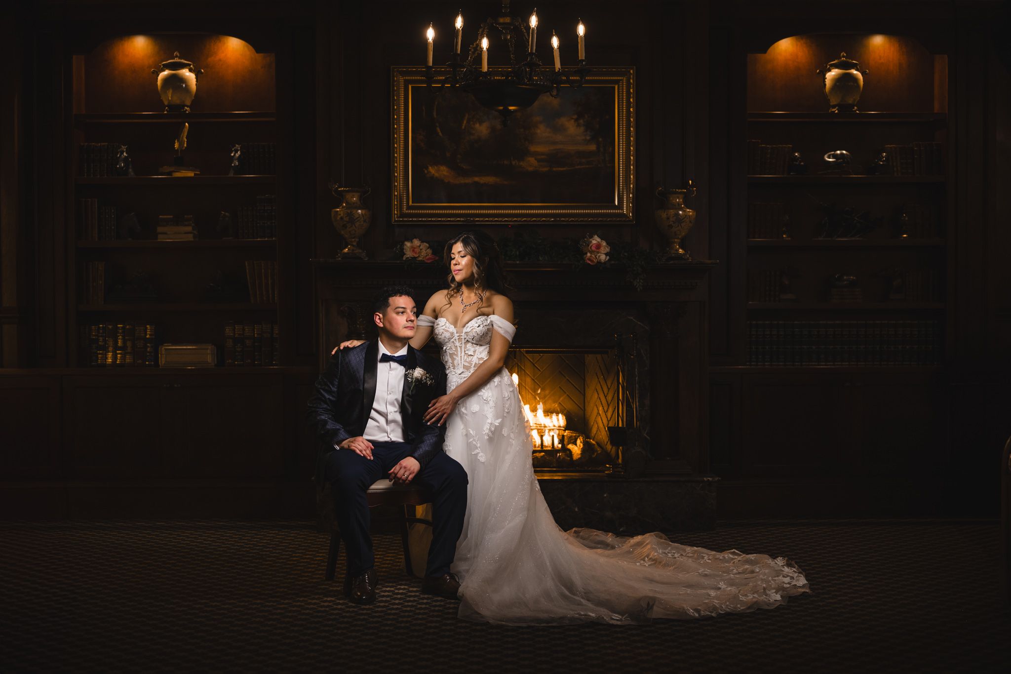 An elegant wedding portrait in a dark, moody setting with candlelight and classic decor.