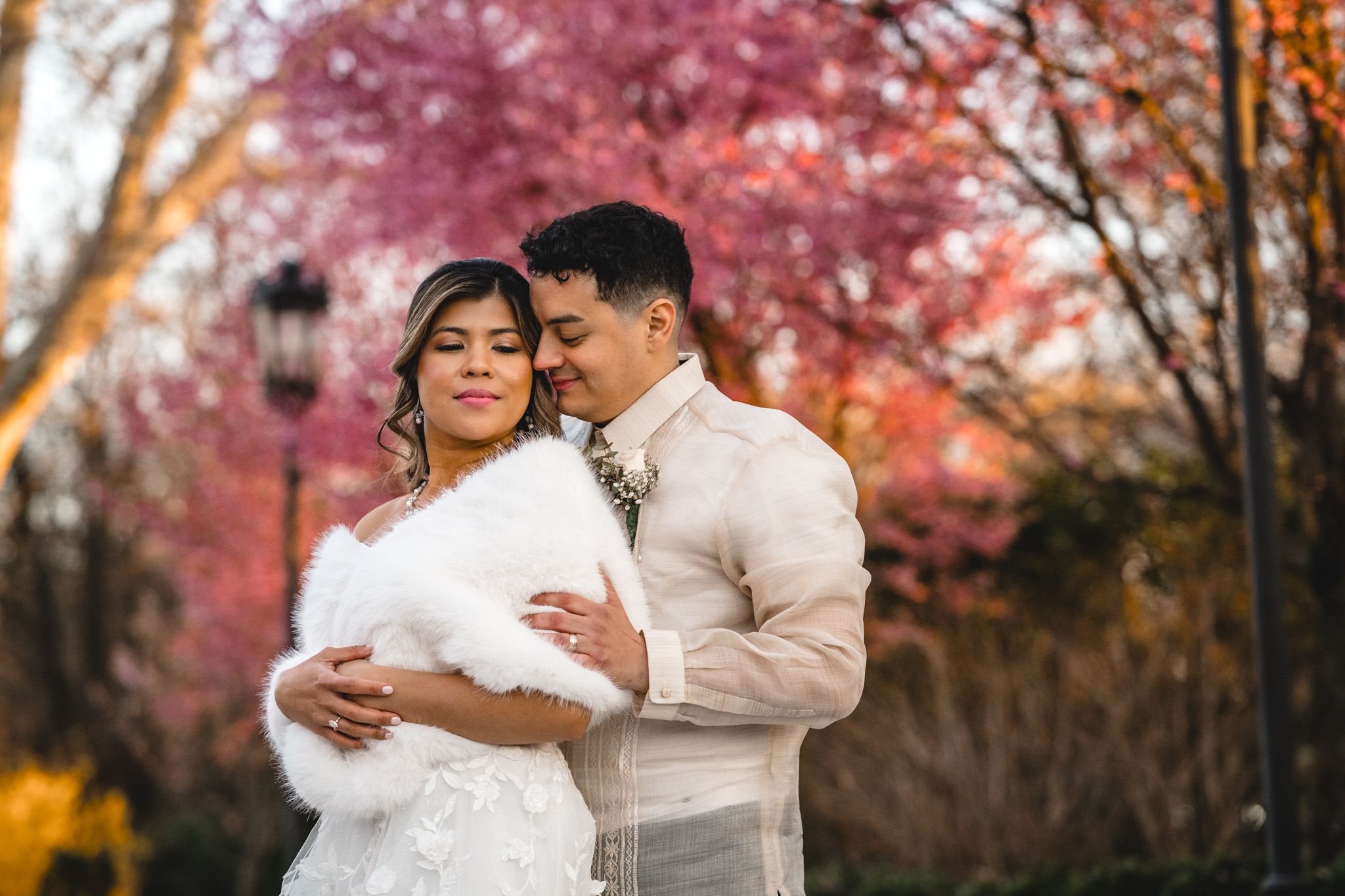 A tender autumn wedding portrait with cherry blossoms and warm lighting in the background.