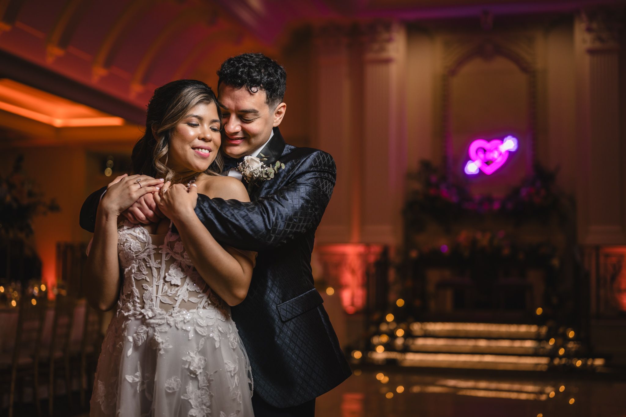 A joyful couple dancing together at their wedding reception with pink ambient lighting.