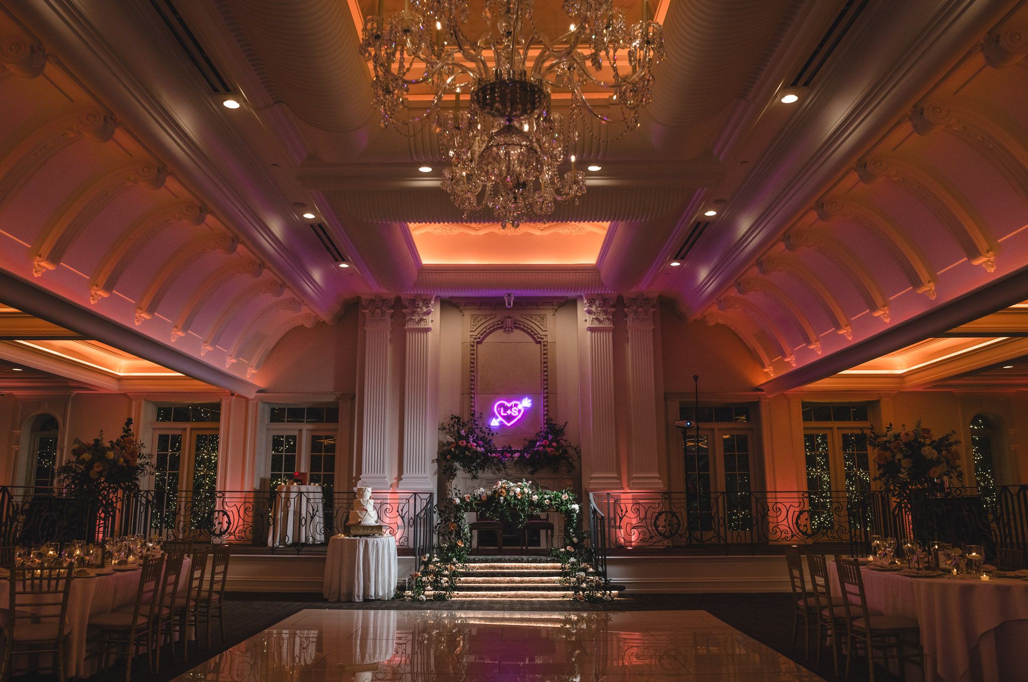 An empty wedding reception ballroom with pink uplighting and a crystal chandelier.