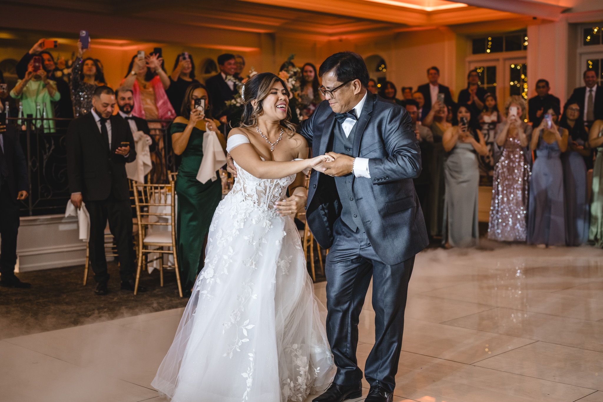 A couple performs their wedding dance in a beautifully lit ballroom surrounded by guests.