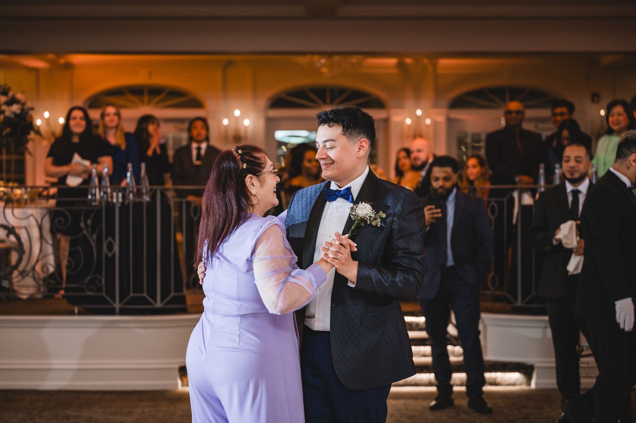 A couple shares their first dance at an elegant wedding reception with warm lighting and onlooking guests.