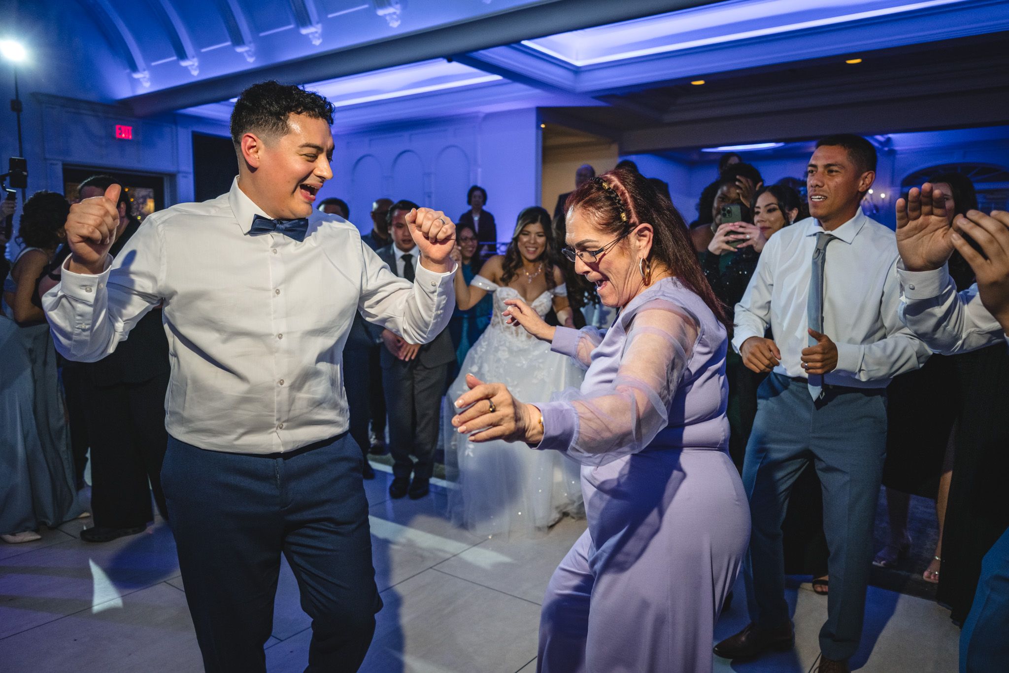 Guests dancing energetically at wedding reception under blue lighting.