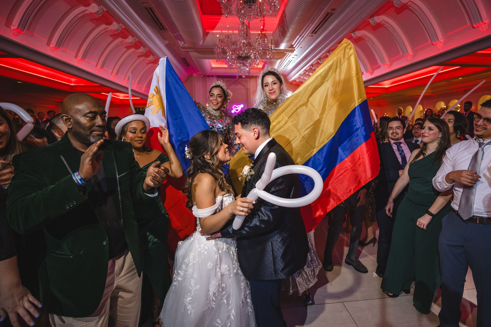 Wedding celebration features Colombian flag and dancing crowd in vibrant red-lit ballroom.