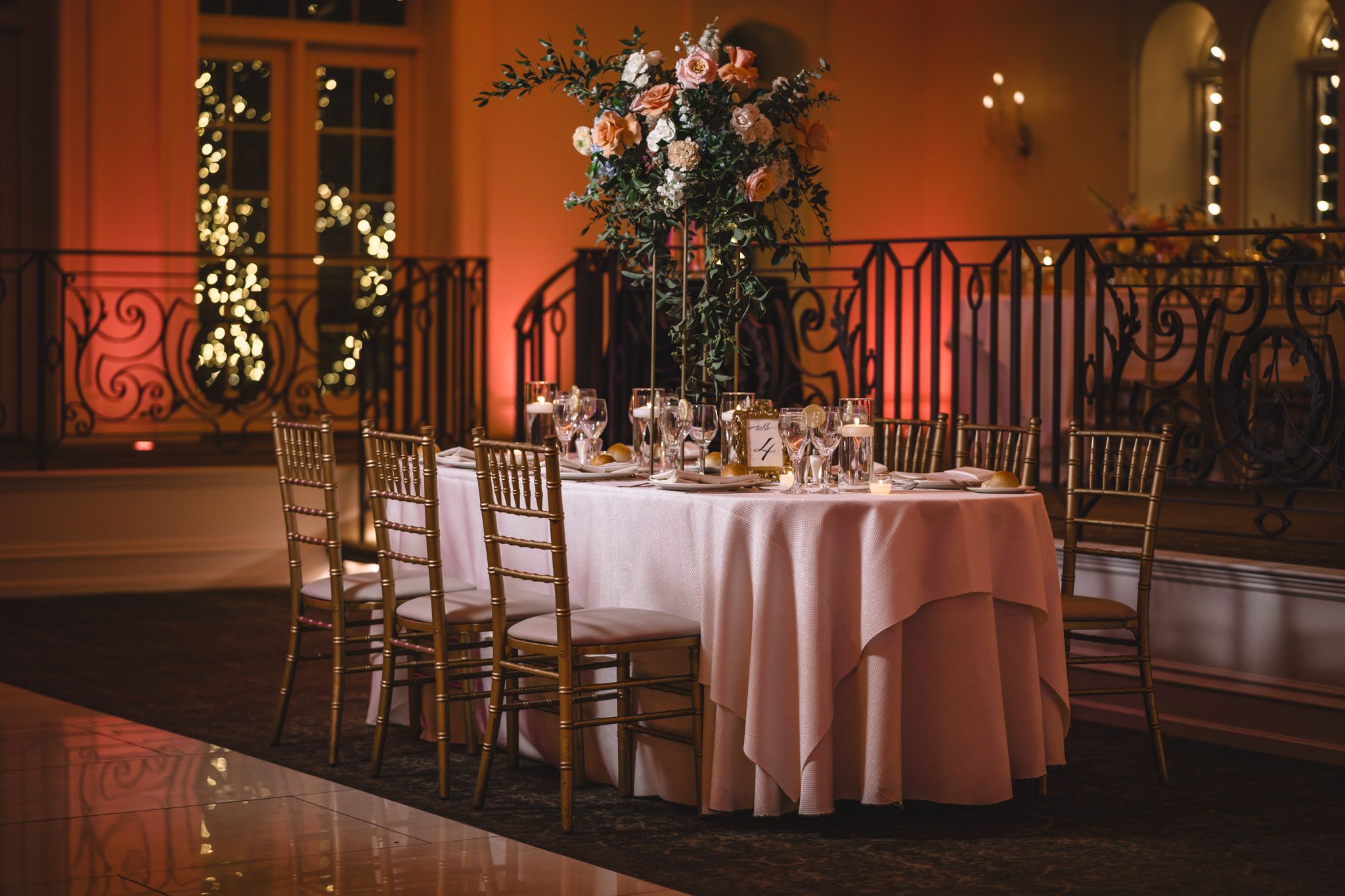 Elegant ballroom reception setup with pink uplighting and floral centerpieces on round tables.
