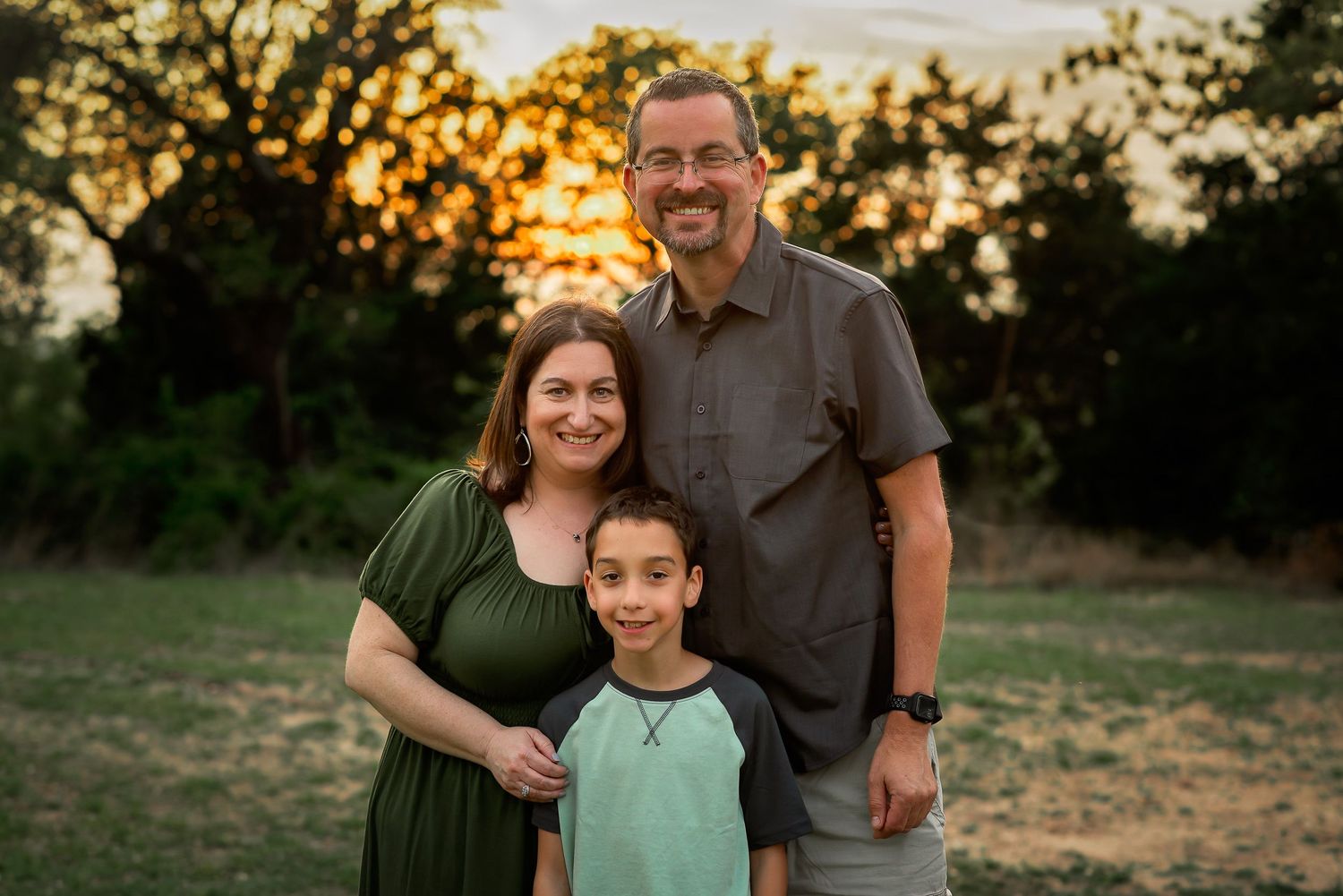 family of three, posing with sunset behind them for portrait session