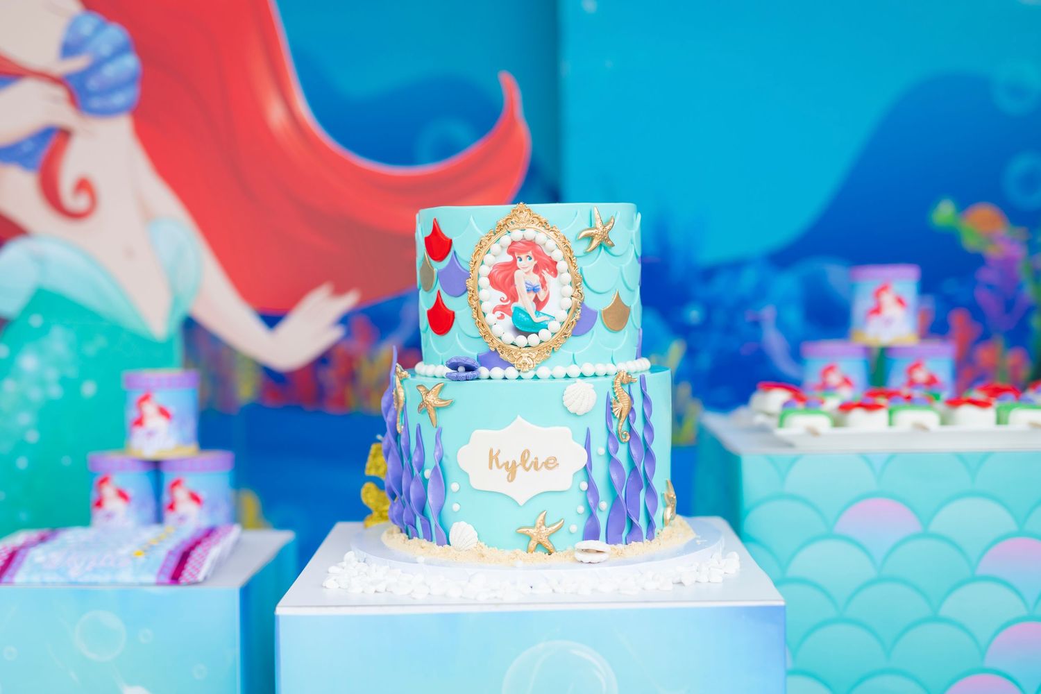 Little Mermaid themed birthday cake with blue and teal decorations on display.