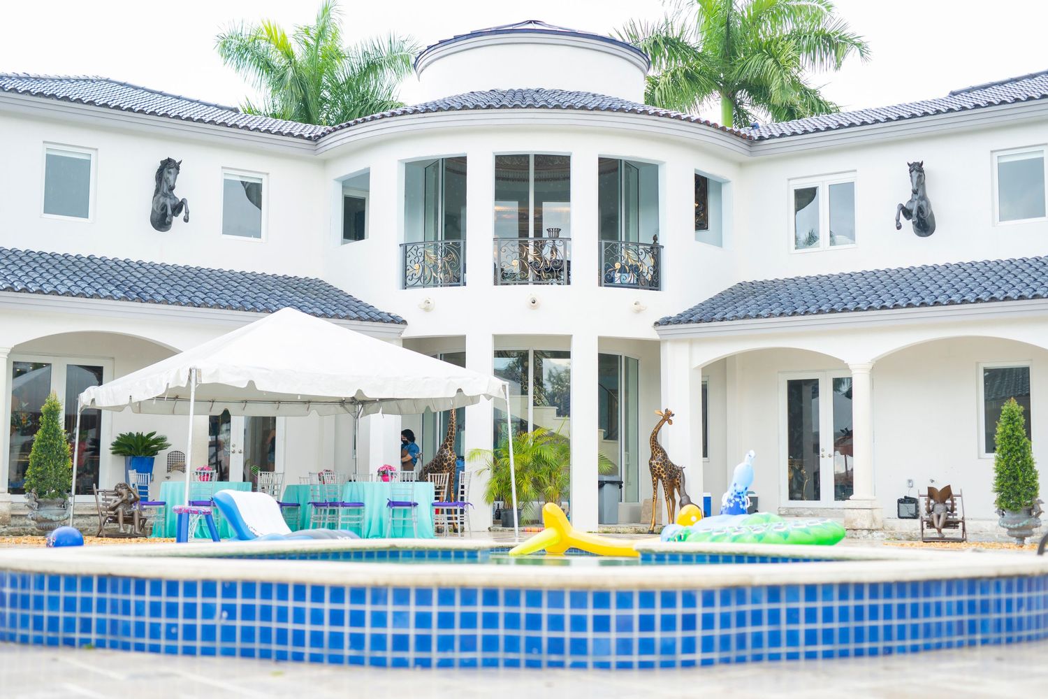 Luxury white mansion with blue-tiled pool and outdoor party setup.