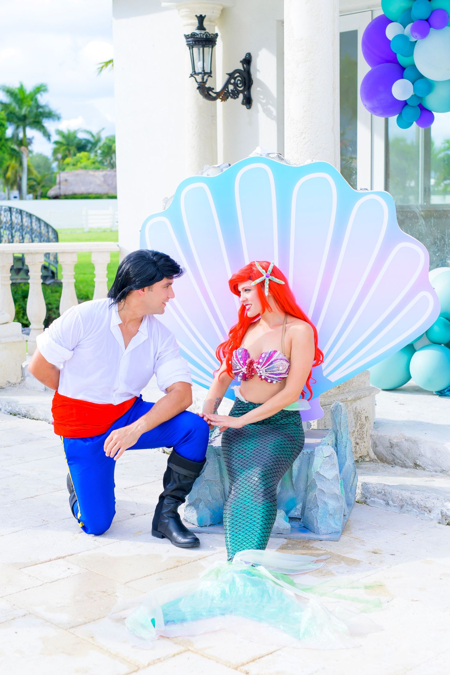 Costumed performers pose by large decorative seashell backdrop with blue balloons.