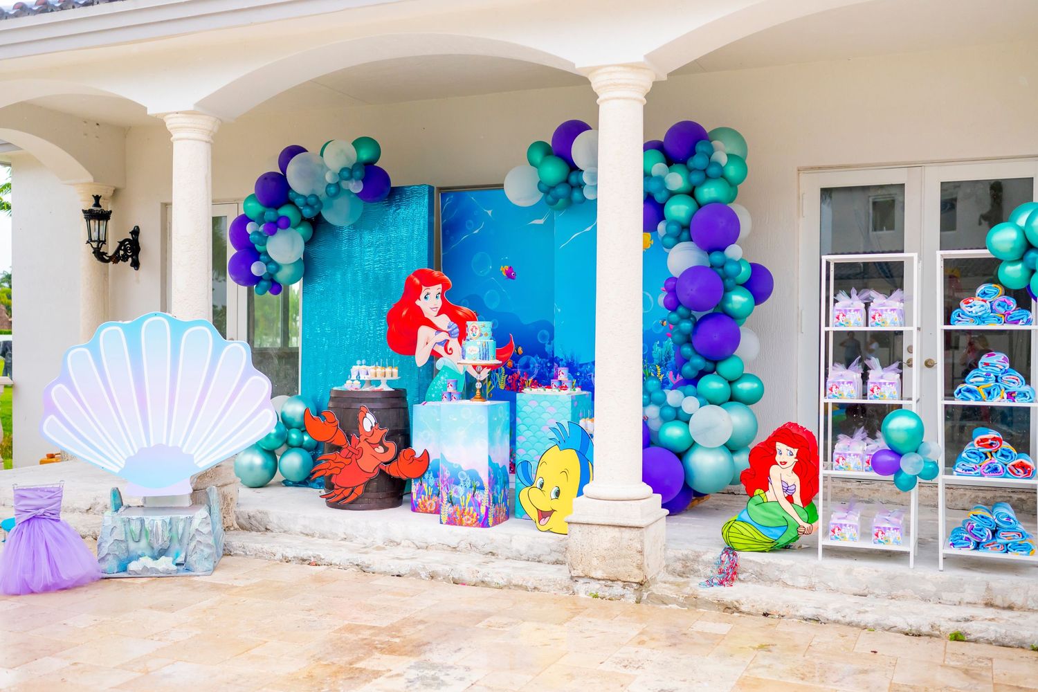 Mermaid themed party setup with balloon arch, seashell backdrop and underwater decorations.