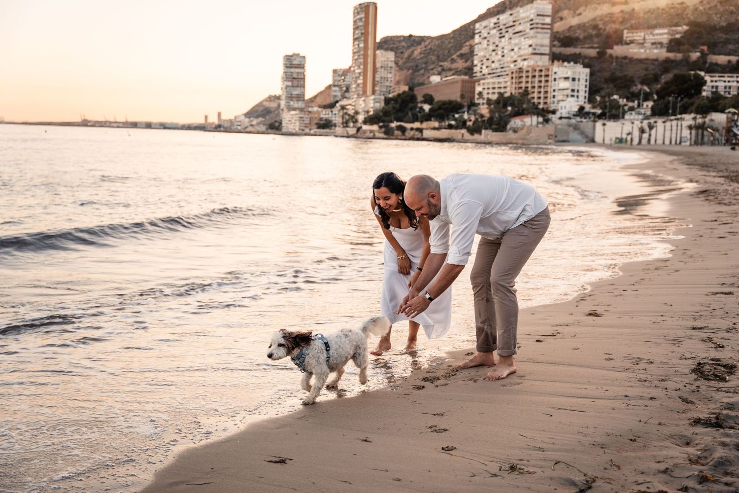 Couple chasing dog and smiling on the beach at sunset for a photo shoot on the beach in Alicante