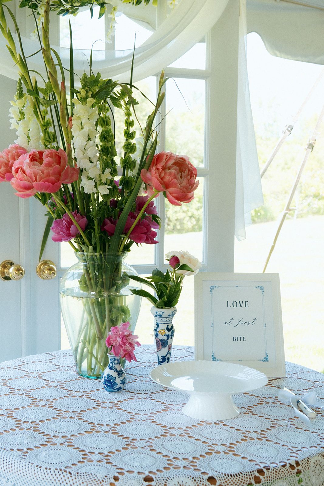 Elegant floral centerpiece with pink and white flowers in a glass vase on lace tablecloth.