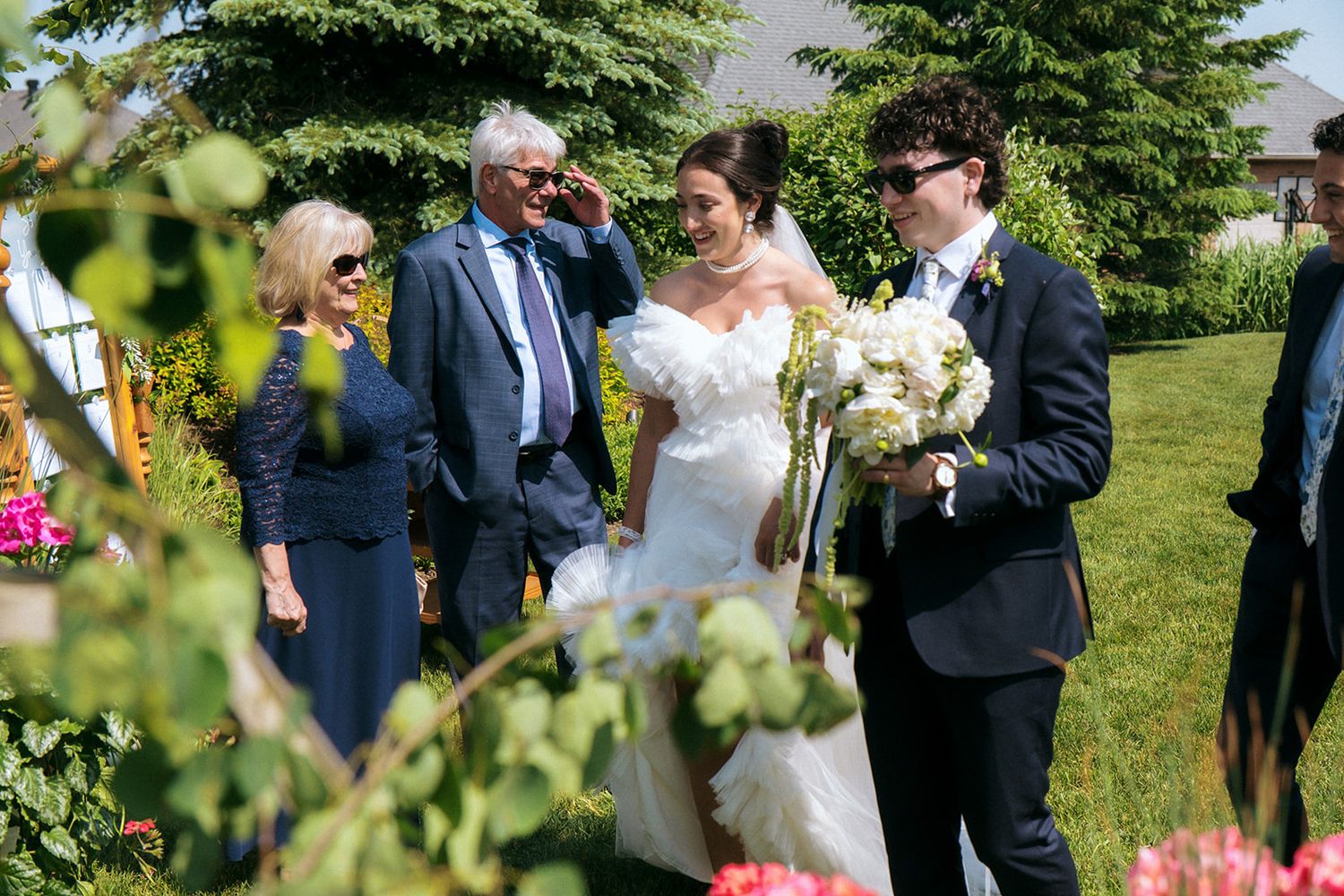 Outdoor wedding ceremony scene with guests gathered in sunny garden setting.