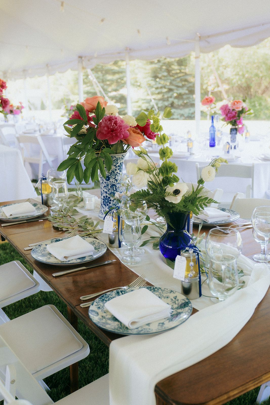 Wedding reception table with blue and white china place settings and vibrant floral centerpieces.