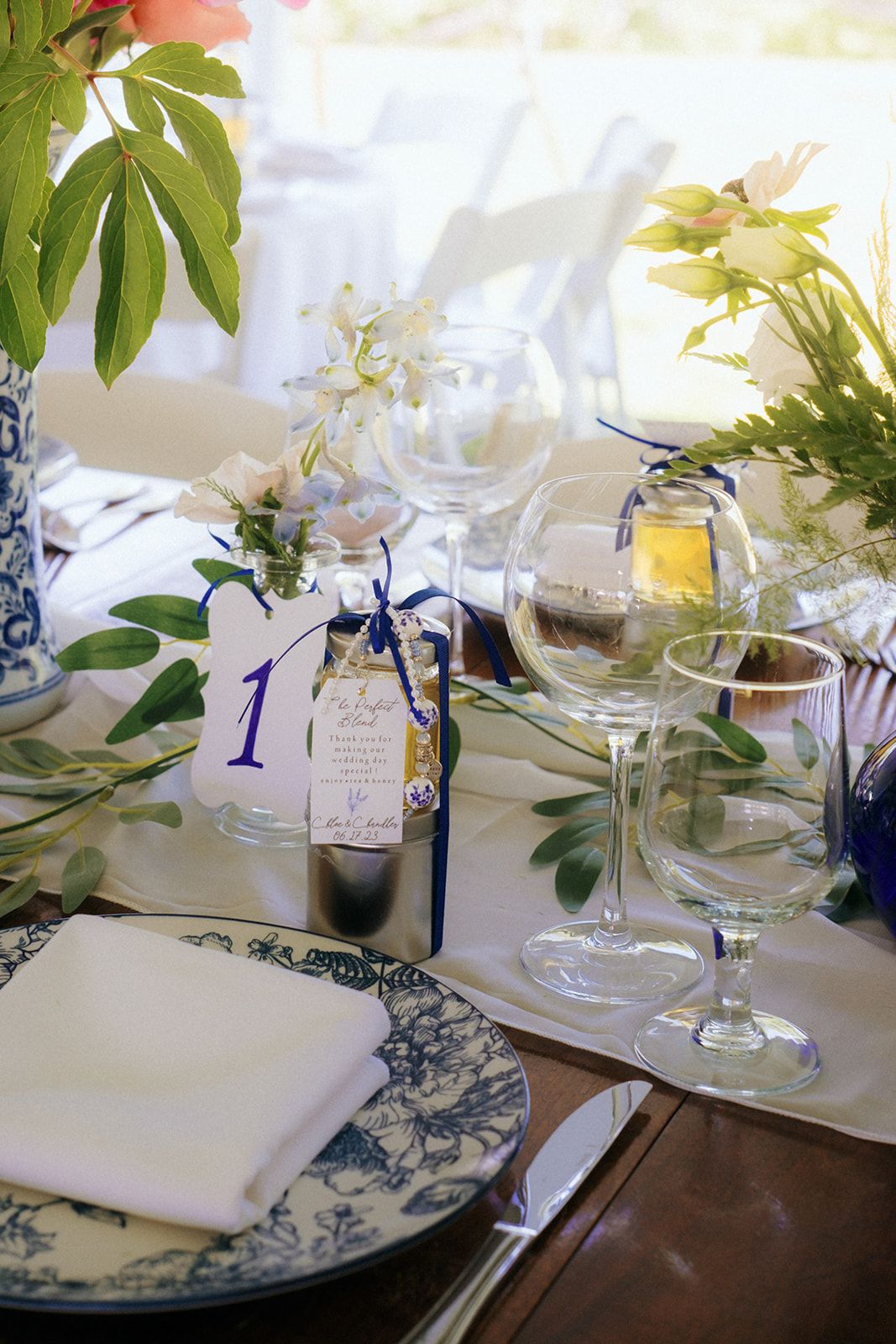 Elegant place settings with blue and white china plates, flowers, and table decor at an outdoor wedding reception.