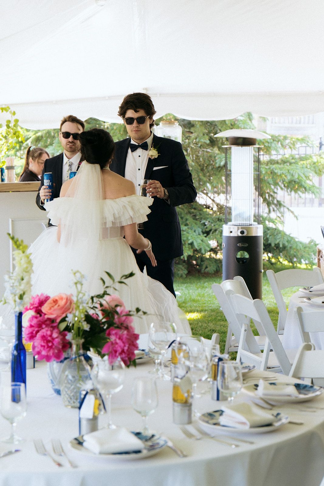 Wedding reception tables set with white linens and bright pink floral centerpieces under an outdoor tent.