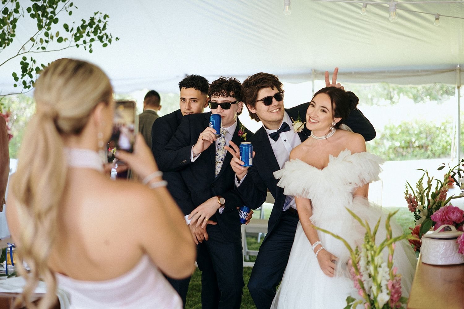 Outdoor wedding celebration with guests mingling under white tent canopy.