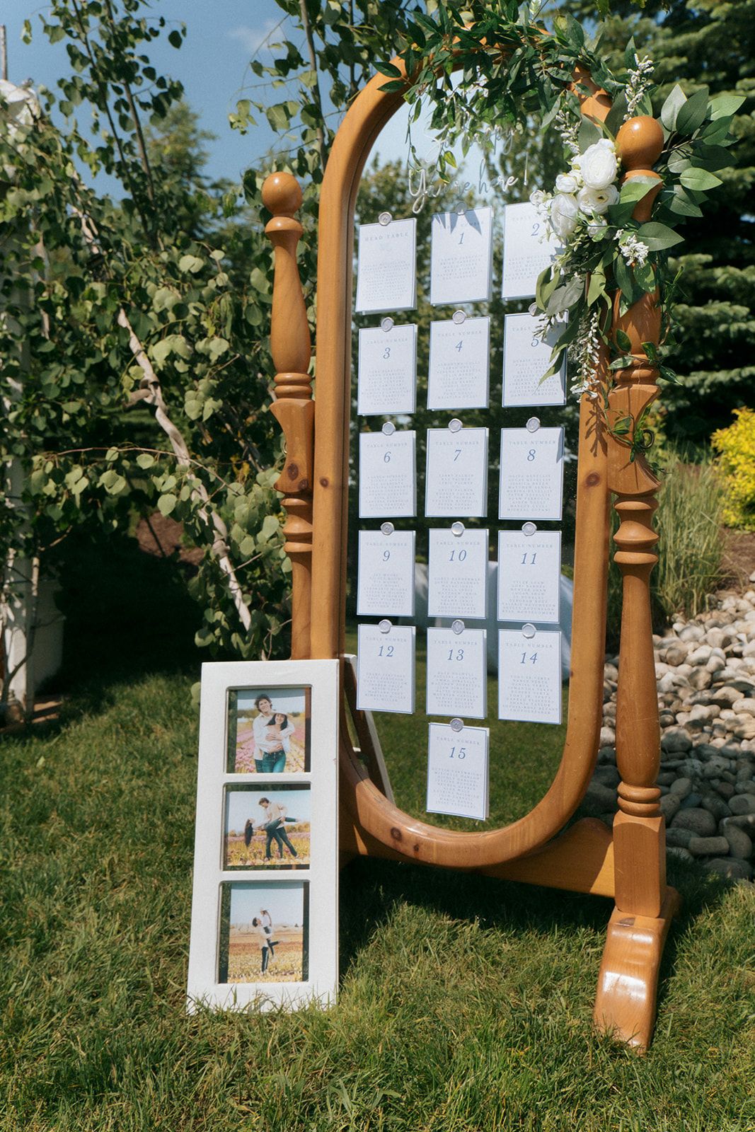 Wooden frame seating chart display with photo frames on grass at outdoor event.
