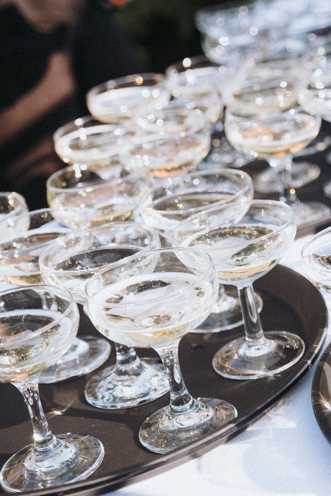 Rows of champagne coupe glasses arranged on dark serving trays at formal event.