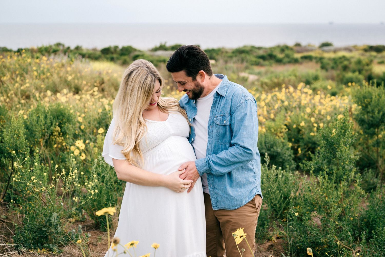 Couple embraces in a wildflower meadow as they pose for romantic maternity photos at sunset.