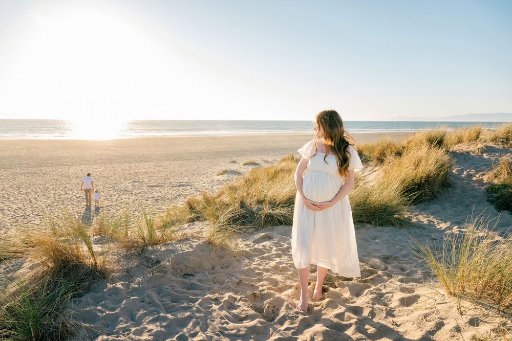 A person in a white dress walks along a sandy beach path during golden hour at sunset.
