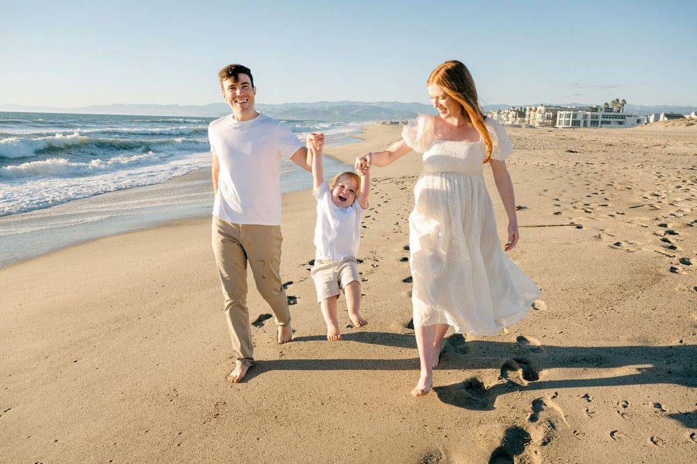 Family walking along sandy beach at sunset holding hands and leaving footprints in golden sand.