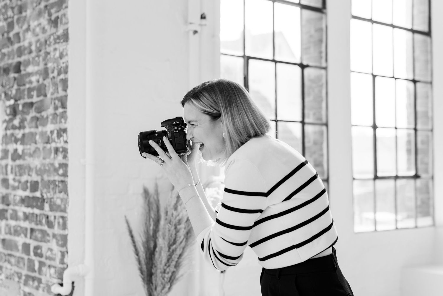 Photographer in striped shirt capturing moments in bright industrial studio space.