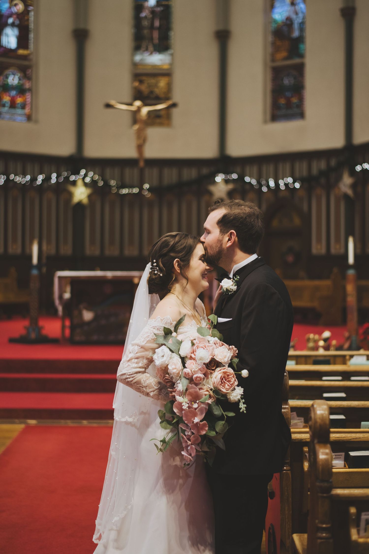 a groom kisses his bride on the forehead while standing inside of st andrew's cathedral in victoria british columbia.