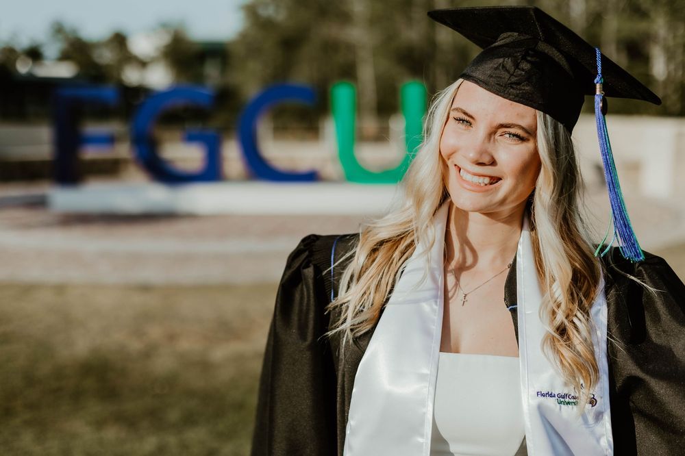 Graduate in white dress and cap smiles during outdoor graduation photos.
