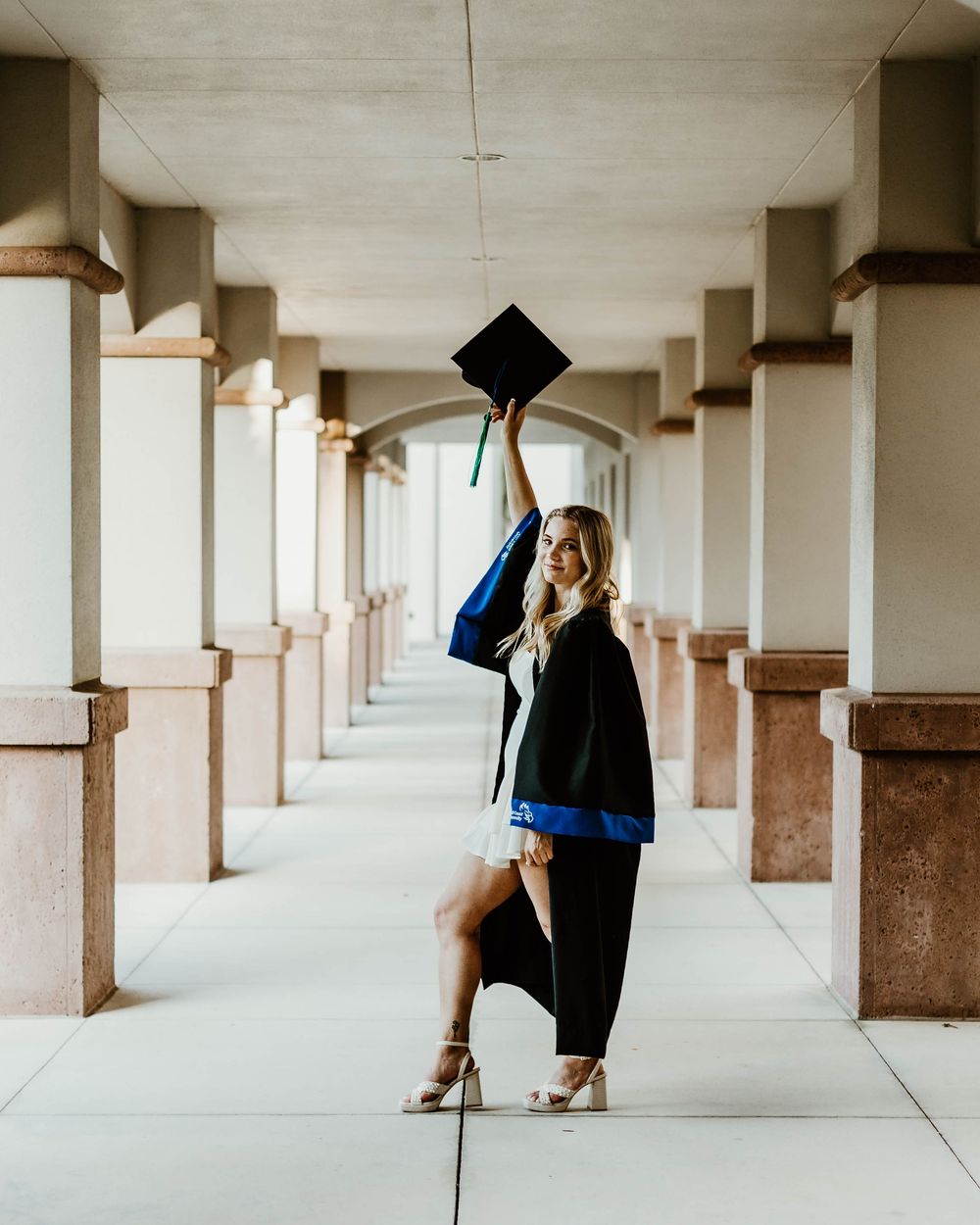 Graduate celebrates in covered walkway with pillars and white architecture.